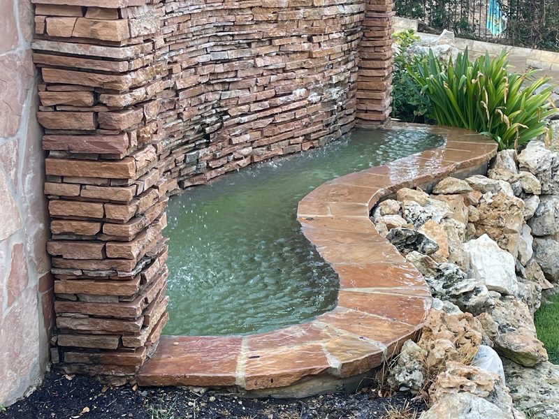 A stone wall water feature spilling into a pool